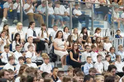 Grupa dzieci w białych koszulach i nauczycieli na szkolnej uroczystości.