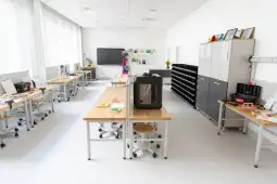 Nowoczesna pracownia z biurkami, drukarką 3D i materiałami do nauki.
