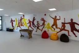 Kolorowe sylwetki sportowców na ścianie oraz pufy w różnych kolorach.