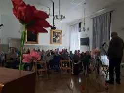 Spotkanie grupy osób w sali, z kwiatami w pierwszym planie.