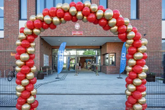 Łuk balonowy w kolorach czerwonym i złotym przy wejściu do budynku.