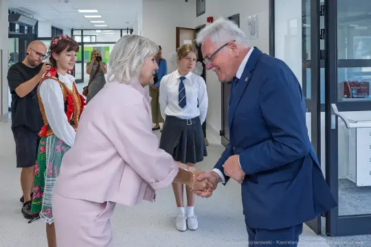 Spotkanie dwóch osób podczas ceremonii, w tle młodzież w strojach szkolnych i ludowych.