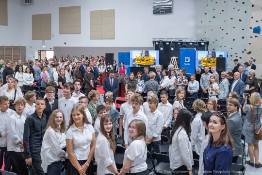 Tłum ludzi w białych koszulach na wydarzeniu w sali z dekoracjami.