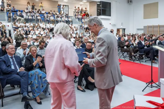 Wręczenie dyplomu podczas uroczystości akademickiej z udziałem publiczności.