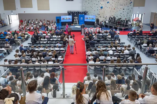 Uroczystość w sali, z uczestnikami siedzącymi na widowni i wystąpieniami na scenie.