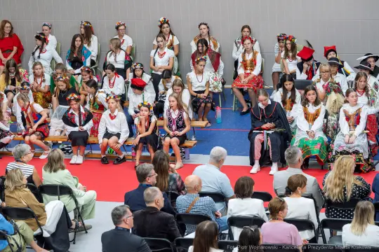 Grupa dzieci w tradycyjnych strojach ludowych podczas występu na scenie.