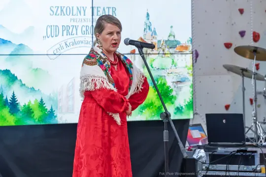 Kobieta w tradycyjnym stroju ludowym śpiewa do mikrofonu na tle sceny.