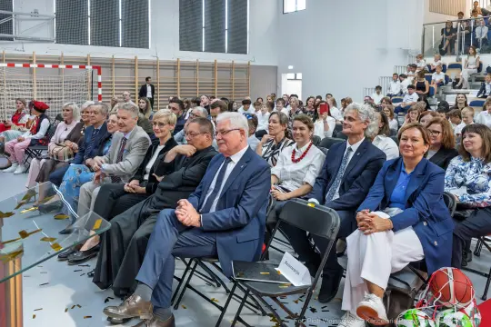 Grupa ludzi siedzących na widowni podczas wydarzenia w sali sportowej.
