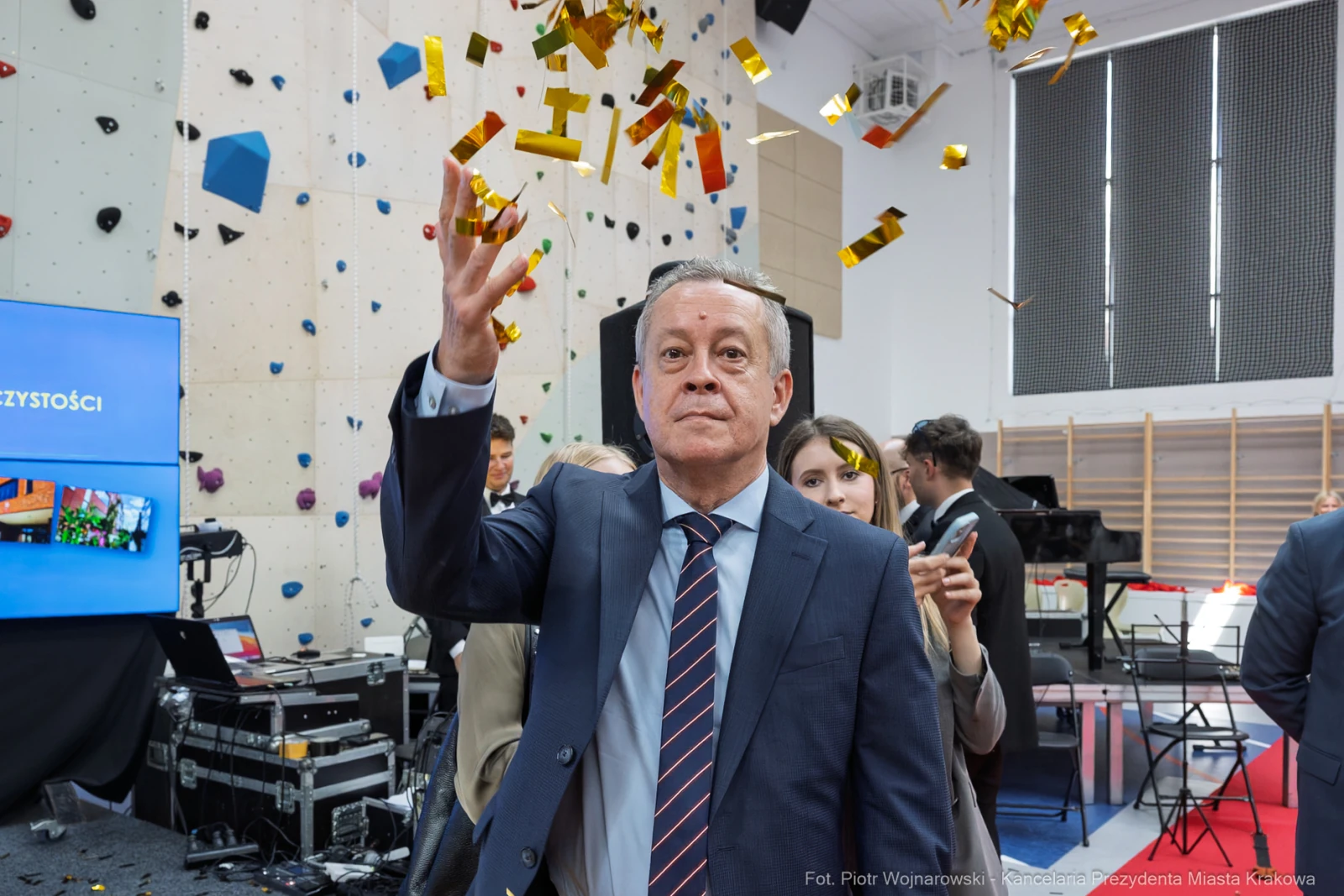 Mężczyzna w garniturze rzuca konfetti w sali pełnej ludzi.  Autor: Piotr Wojnarowski