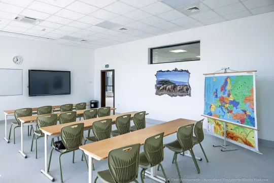 Nowoczesna sala lekcyjna z biurkami, tablicą interaktywną i mapą Europy.