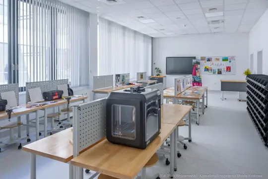 Nowoczesna pracownia z drukarką 3D, stołami i materiałami do pracy.