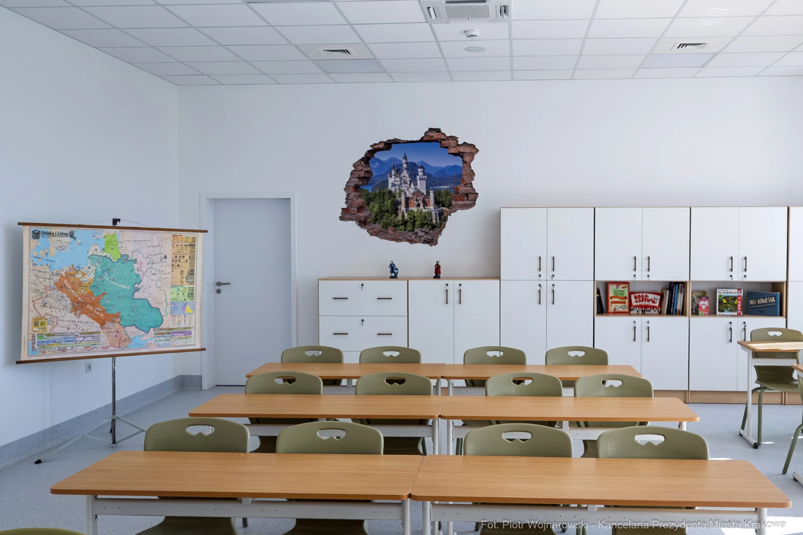 Pusty pokój lekcyjny z mapą na tablicy i uszkodzoną ścianą z widokiem na zamek.  Autor: Piotr Wojnarowski