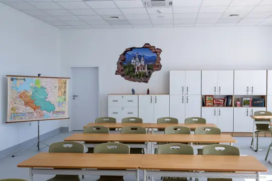 Pusty pokój lekcyjny z mapą na tablicy i uszkodzoną ścianą z widokiem na zamek.