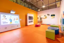 Nowoczesna sala zabaw dla dzieci z interaktywnymi ekranami i kolorowymi meblami.