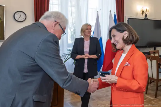 Spotkanie dwóch osób przy uścisku dłoni, w tle kobieta w garniturze.