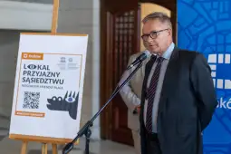 Mężczyzna przemawia przy tablicy informacyjnej o lokalach przyjaznych sąsiedztwu.
