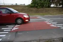 Czerwony samochód przejeżdża przez wyniesioną strefę przejścia dla pieszych.