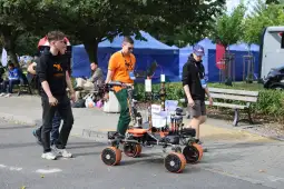 Grupa młodych ludzi prowadzi robota marsjańskiego na festiwalu technologii.