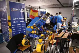 Robot z elementami elektronicznymi w warsztacie, w tle zespół pracujący nad projektami.