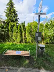 Ławka przystankowa z tabliczką informującą o zakazie korzystania. W tle żywopłot.