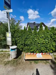 Ławka przystankowa z tabliczką informującą o remoncie, otoczona zielenią.