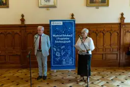Dwójka mówców przy mikrofonach, w tle baner Wydziału Edukacji i Projektów Edukacyjnych w Krakowie.