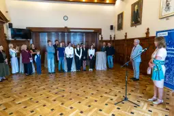 Uczestnicy wydarzenia edukacyjnego w sali z drewnianymi elementami i obrazami na ścianach.