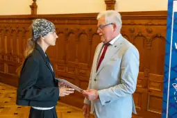 Młoda kobieta rozmawia z mężczyzną w garniturze, trzymając dokumenty.