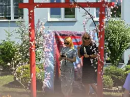 Dwie kobiety w eleganckich strojach przechodzą przez ozdobną bramę z kwiatami.
