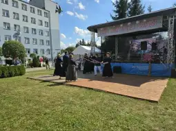 Grupa osób w tradycyjnych strojach wykonuje pokaz sztuk walki na scenie plenerowej.