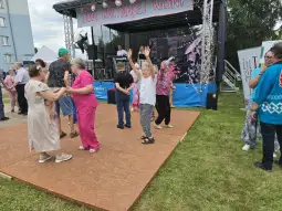 Grupa osób tańczących na scenie podczas wydarzenia plenerowego.