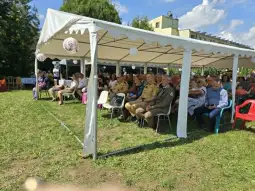 Grupa ludzi siedzących pod namiotem na wydarzeniu plenerowym.