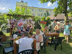 Grupa osób bawiących się w ogrodzie, tworzących dekoracje z kwiatów.