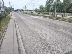 Pusta ulica z torami tramwajowymi i oznakowaniem drogowym.