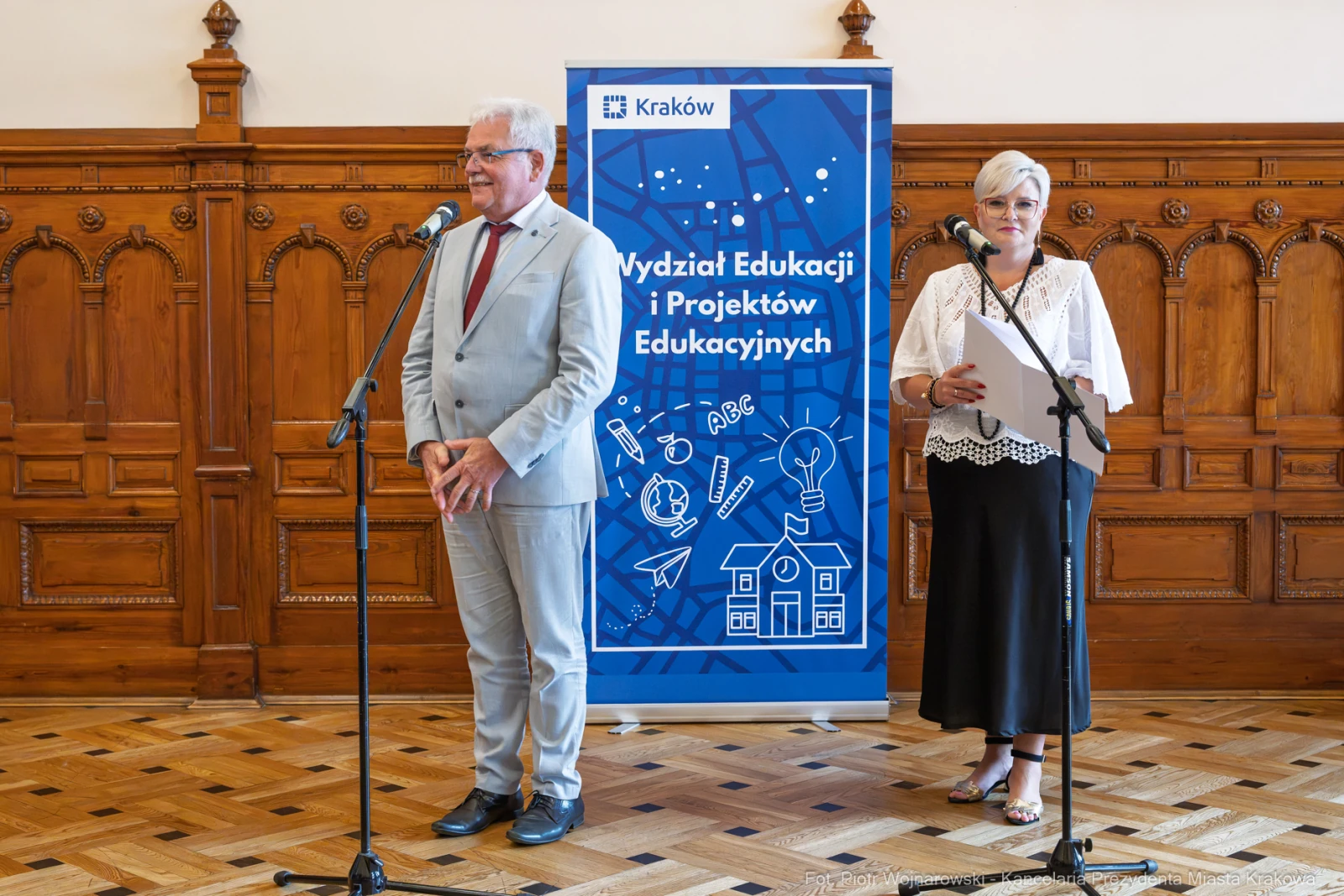Dwójka mówców przy mikrofonach, w tle baner Wydziału Edukacji i Projektów Edukacyjnych.  Autor: Piotr Wojnarowski