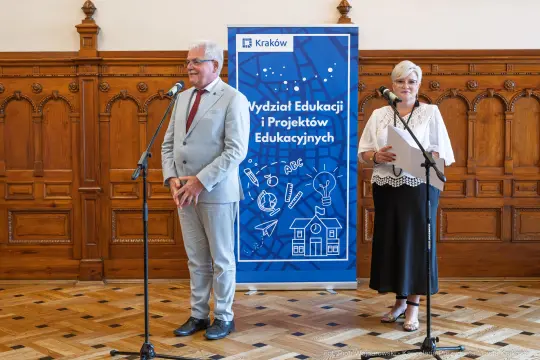 Dwójka mówców przy mikrofonach, w tle baner Wydziału Edukacji i Projektów Edukacyjnych.