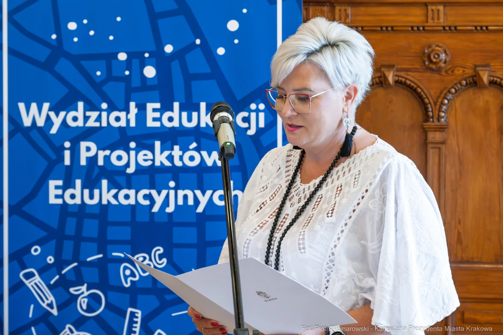 Kobieta czytająca z kartki przy mikrofonie, w tle plakat z logo Wydziału Edukacji.  Autor: Piotr Wojnarowski