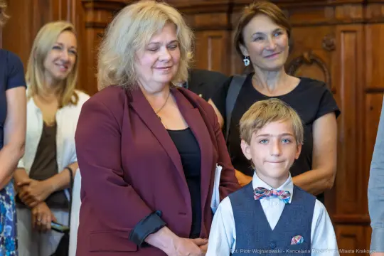 Grupa osób w formalnych strojach, w tym chłopiec w kamizelce i muszce.