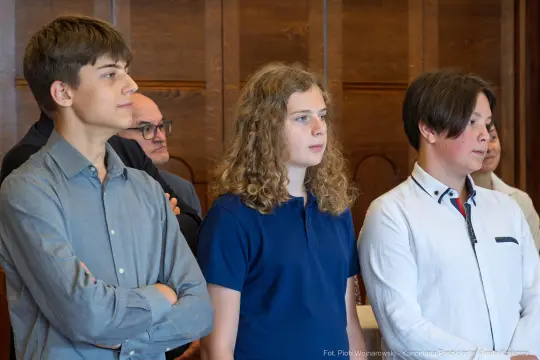 Grupa młodych ludzi w formalnych strojach, skupionych na wydarzeniu.