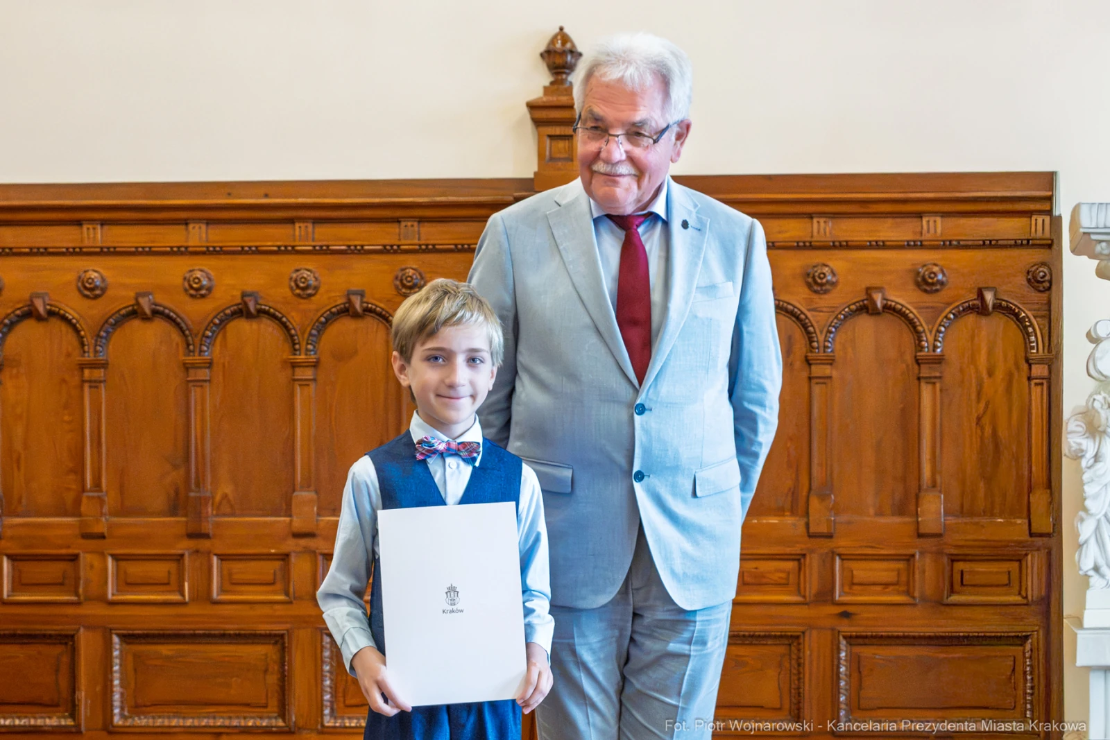 Chłopiec w eleganckim stroju trzyma dyplom, obok stoi starszy mężczyzna w garniturze.  Autor: Piotr Wojnarowski