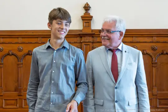 Młody mężczyzna i starszy mężczyzna uśmiechają się, stojąc obok siebie w eleganckim wnętrzu.