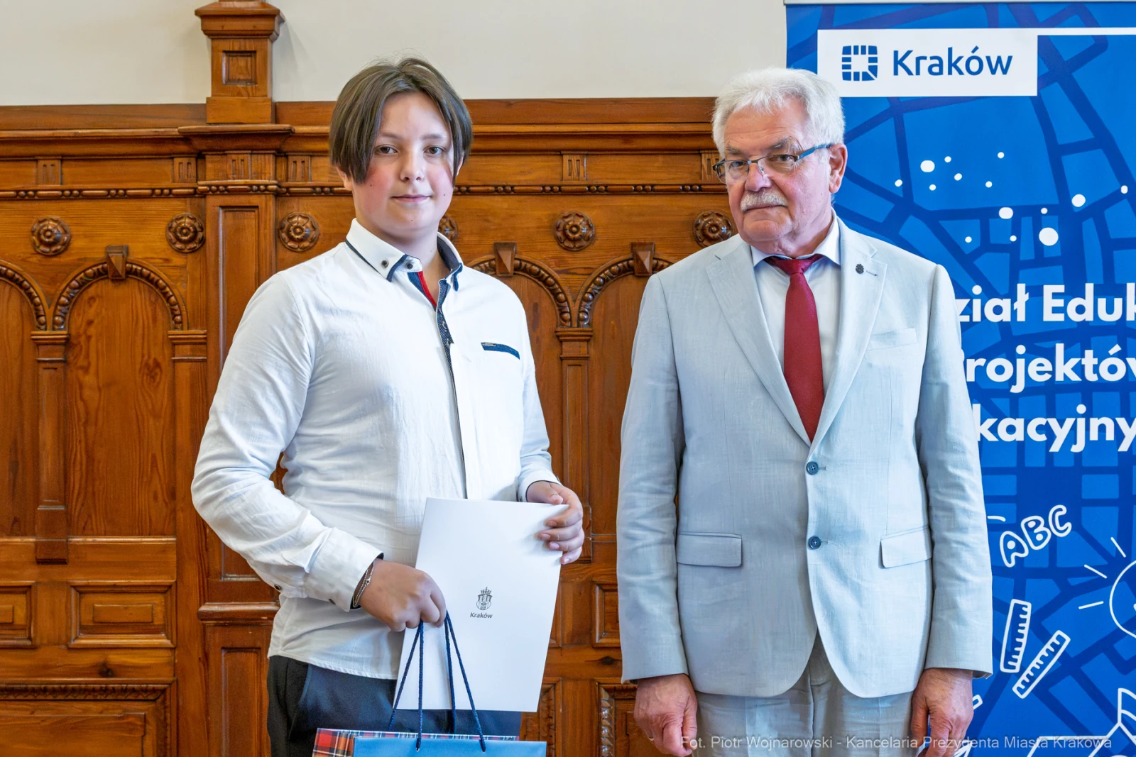 Młody mężczyzna z dyplomem stoi obok starszego mężczyzny w garniturze.  Autor: Piotr Wojnarowski