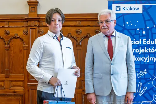 Młody mężczyzna z dyplomem stoi obok starszego mężczyzny w garniturze.