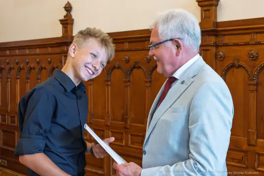 Młody chłopak uśmiecha się do starszego mężczyzny w eleganckim otoczeniu.