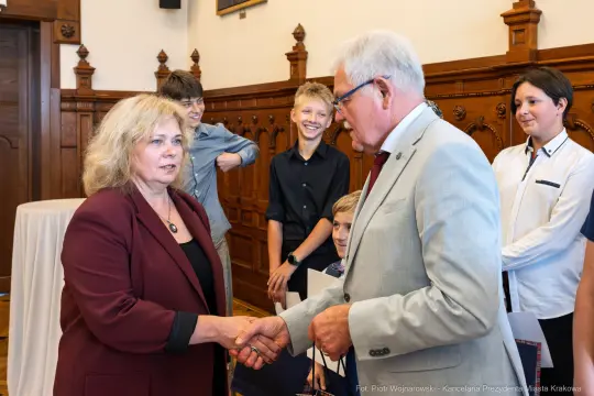 Spotkanie dwóch osób, uściski dłoni, w tle grupa młodych ludzi.