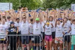 Biegacze w koszulkach sportowych trzymają ręce w górze przed startem biegu.