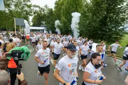 Biegacze w koszulkach startowych uczestniczą w wydarzeniu biegowym w otoczeniu zieleni.