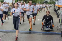 Biegacze i zawodnik na wózku inwalidzkim podczas zawodów biegowych.
