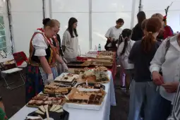 Kobiety w tradycyjnych strojach serwują różnorodne ciasta na festynie.