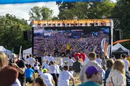 Tłum ludzi uczestniczących w wydarzeniu na świeżym powietrzu z dużym ekranem.